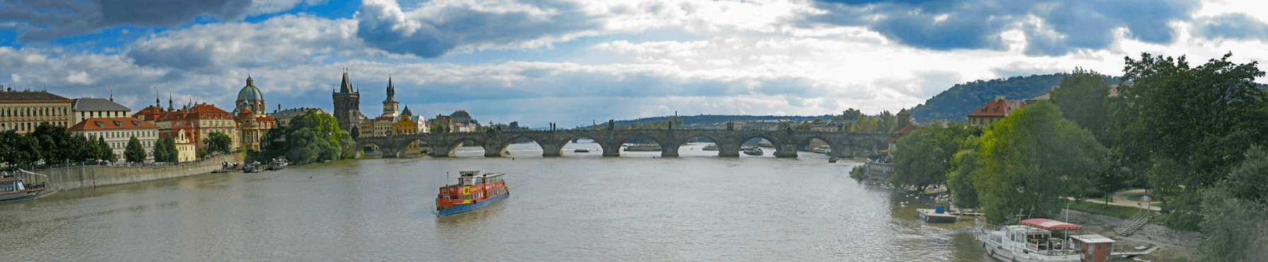 View of Prague and River with a boat navigating towards a bridge